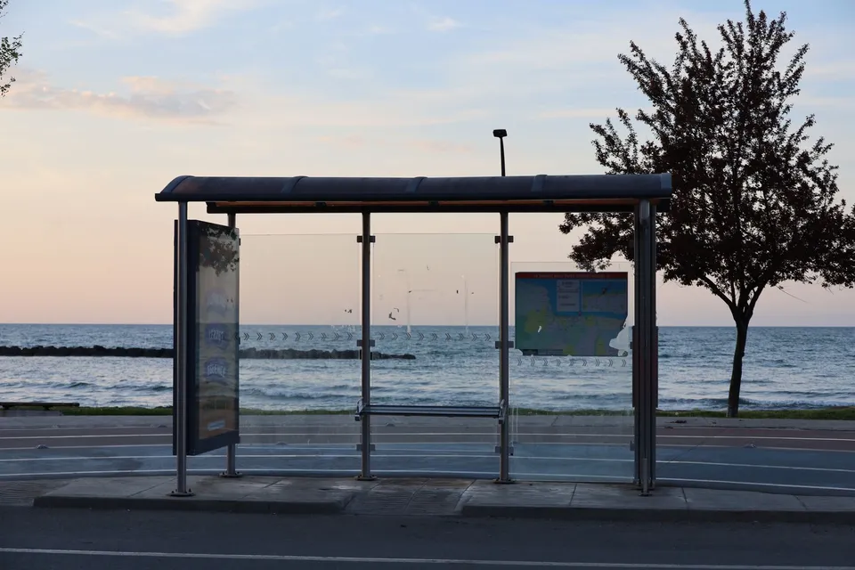 Empty bus stop by the sea at dusk, serene ocean and sky backdrop.