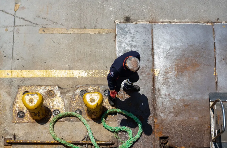 Overhead view of a dock worker handling a mooring rope on a sunny day.