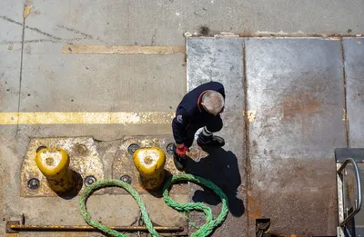 Overhead view of a dock worker handling a mooring rope on a sunny day.